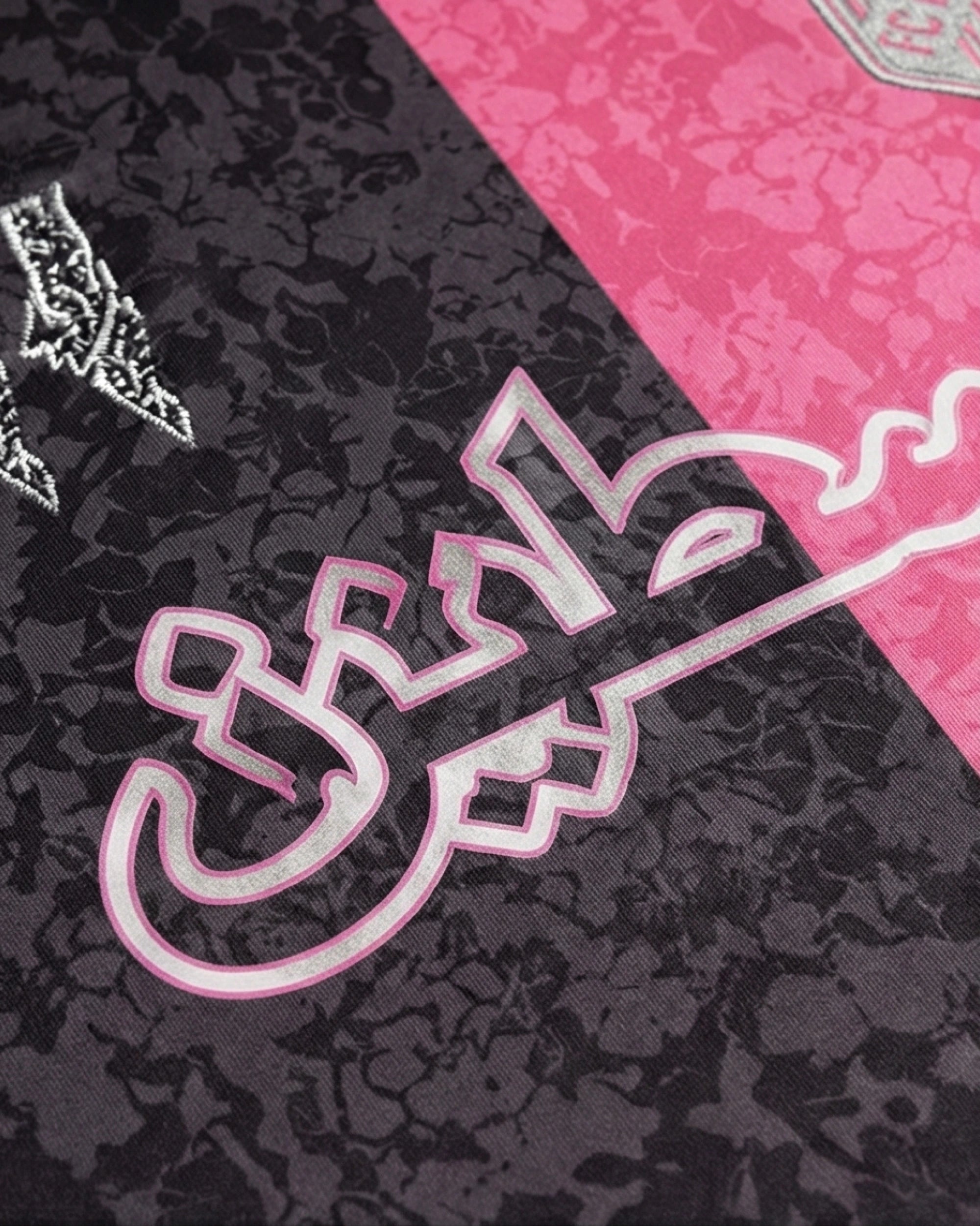 Détail du maillot Palestine noir et rose avec typographie arabe sur fond floral bicolore.